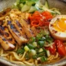 Top-down view of a bowl of chicken ramen with noodles, chicken, vegetables, and a soft-boiled egg